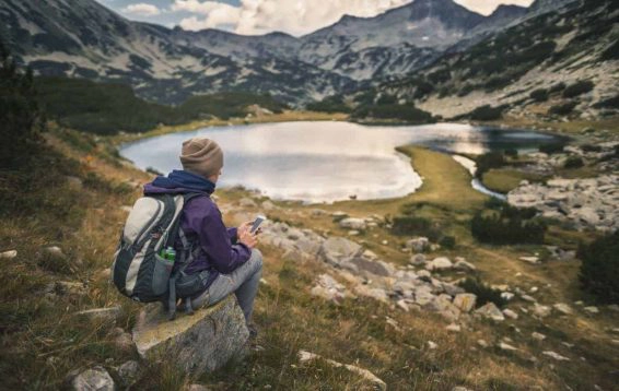 Traveler using a smart phone in mountains sitting near lake