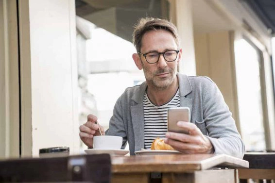 Portrait of mature man sitting at sidewalk cafe looking at cell phone