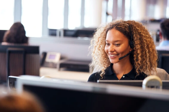 Young businesswoman wearing telephone headset talking to caller in customer services department