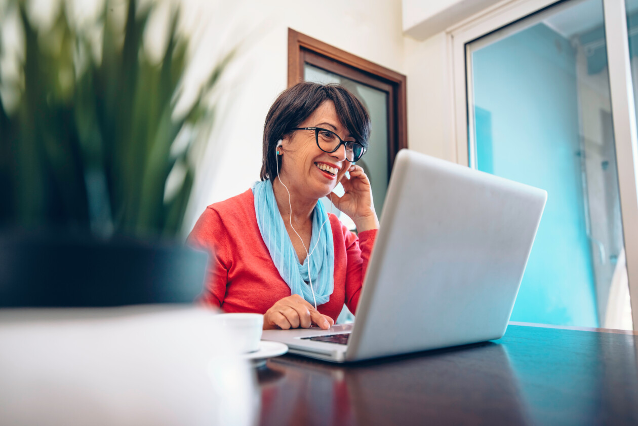 Sixty year old female teacher wearing headphones having online c