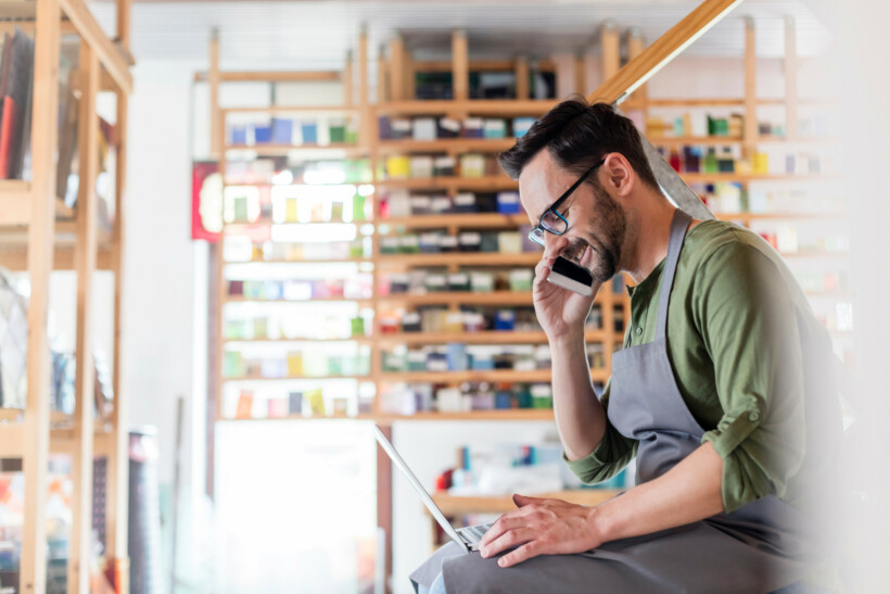 Stained glass artist talking on cell phone and using laptop in studio