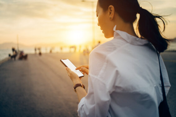 Young lady using smartphone while having a relaxing walk by the pier afterwork at sunset