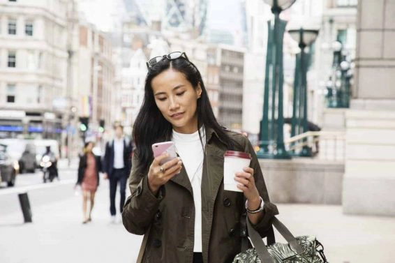 Asian businesswoman looks at smart phone while walking in city.