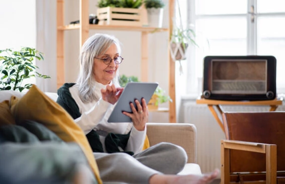 Portrait of senior woman sitting indoors on sofa at home, using tablet.